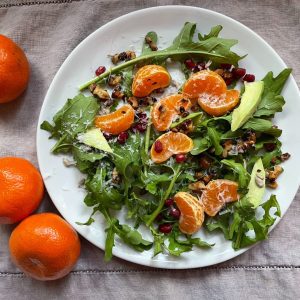 Salad with clementines on a white plate and grey tablecloth