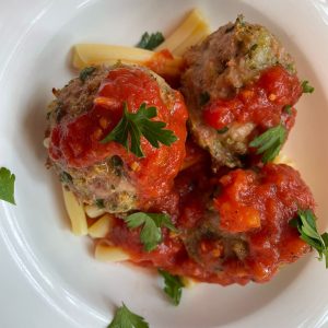 Three meatballs covered in red sauce sit on top of some pasta in a white bowl