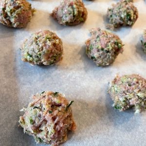 raw meatballs sit on a baking sheet lined with parchment paper