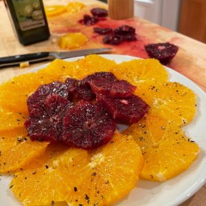 Plate with blood orange slices in a circle, sitting atop bright orange slices also in a circle, sprinkled with pepper