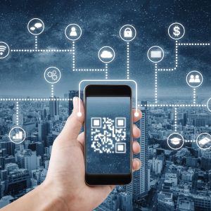 Hand holds a cellphone with a QR code displayed on the screen. In the background is a blue tone image of a city, with icons showing all the things the QR code ostensibly connects to