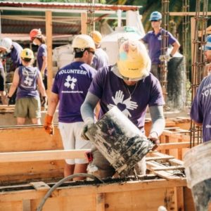 Volunteers wearing matching purple t-shirts and yellow hard hatshelp with a construction project