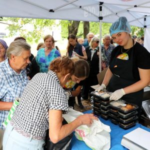 People wait patiently in line for food being distributed by a volunteer in a hair net.