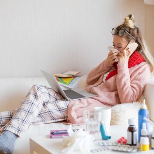 Woman is relaxing on a couch with a bunch of medicines and kleenex on a table next to her