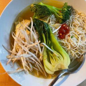 bowl of soup with a light broth, bean sprouts, broccoli, bok choy, noodles, and chili paste