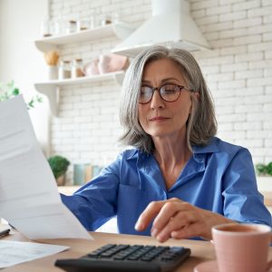 Woman with stylish grey hair looks over paperwork while typing on a calculator