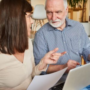 a woman and a man discuss something while looking at papers and a laptop