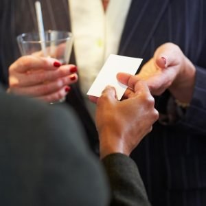 Woman holding a drink is accepting a business card from another woman. Both are in suits, and all we can see are their torsos