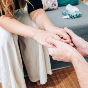 a woman is sitting on the edge of a couch, leaning forward to clasp the hands of someone else. We can see a box of tissues on the couch next to her, as if she's been crying