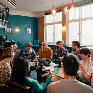 A group of people are gathered in a cafe with books and laptops out on a table in front of them. 