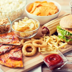 a platter of fast foods like pizza, onion rings, a corn dog, a bowl of ketchup, potato chips, and a burger