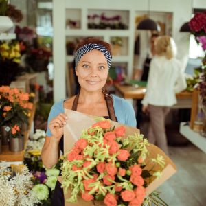 Woman wearing a cloth headband proudly displays a bouquet of flowers in a flower shop