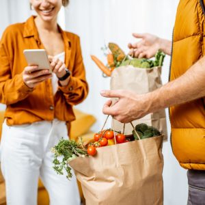 Woman receives the groceries she ordered from a man wearing an orange vest that perfectly matches her orange shirt.