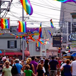 People crowding Commercial Street in Provincetown, MA. Rainbow flags hang overhead