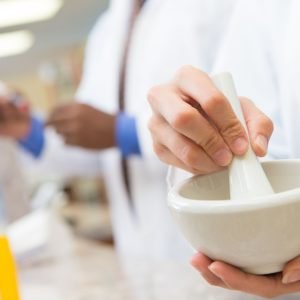 Pharmacist in a white lab coat is compounded a medication with a mortar and pestle