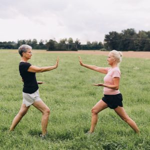 Two women with gray hair practice tai chi together in a field