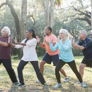 A group of adults practice tai chi in unison outdoors; somewhere with large oak trees and spanish moss