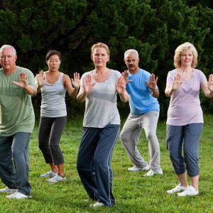 A group of older people practice tai chi postures in a grassy park