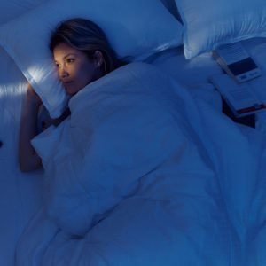 A woman lies awake in bed, seemingly unable to fall asleep.