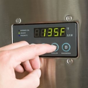 A close-up image of a hand adjusting the temperature setting of a hot water heater
