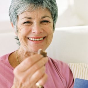 Woman with short, grey hair smiles as she bites into a piece of chocolate