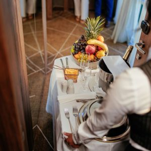 We are looking over the shoulder of a hotel person delivering room service on a wheeled tray cart
