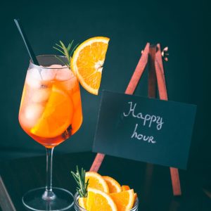 A fruity cocktail with an orange slice garnish sits next to a tiny chalkboard that has "happy hour" written on it
