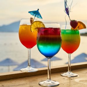 Beautiful, colorful fruity drinks sit on a bartop in front of an ocean view