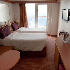 Cruise ship cabin view, with two twin beds in front of a balcony window