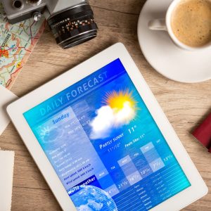 A tablet is opened on a weather forecast site, sitting on a table with a cup of coffee