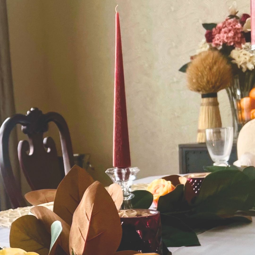 Fall tablescape: a long table set with a garland of magnolia leaves and deep maroon taper candles