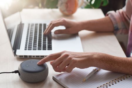 Person using Amazon Alexa device while working on laptop
