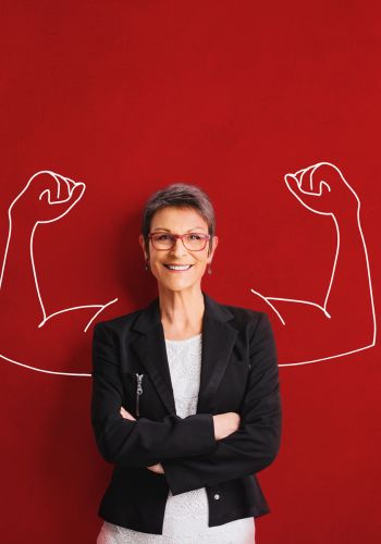 mature woman stands against wall with arms crossed, as an illustration of two strong arms appear behind her